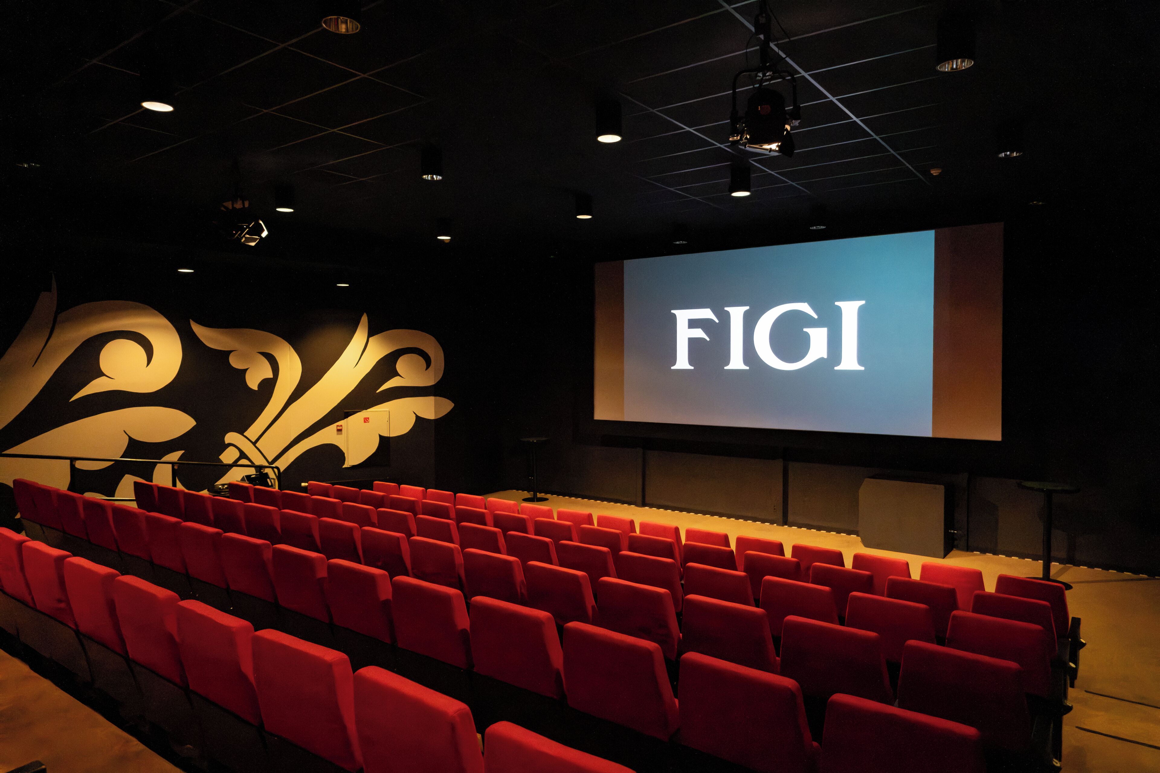 Een auditorium met rode stoelen en een groot scherm waarop 'FIGI' wordt weergegeven.