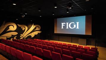 Een auditorium met rode stoelen en een groot scherm waarop 'FIGI' wordt weergegeven.