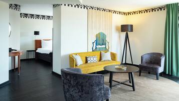 Een hotelkamer met een bed, een gele bank, twee fauteuils, een kleine tafel en een vloerlamp.