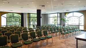 A conference room with rows of green chairs, large windows, and a herringbone patterned floor. - Hotel Theater Figi (Zeist)