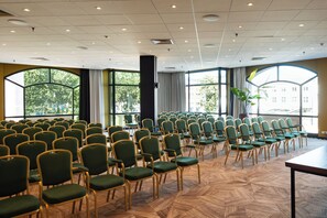 A conference room with rows of green chairs, large windows, and a herringbone patterned floor. - Hotel Theater Figi (Zeist)