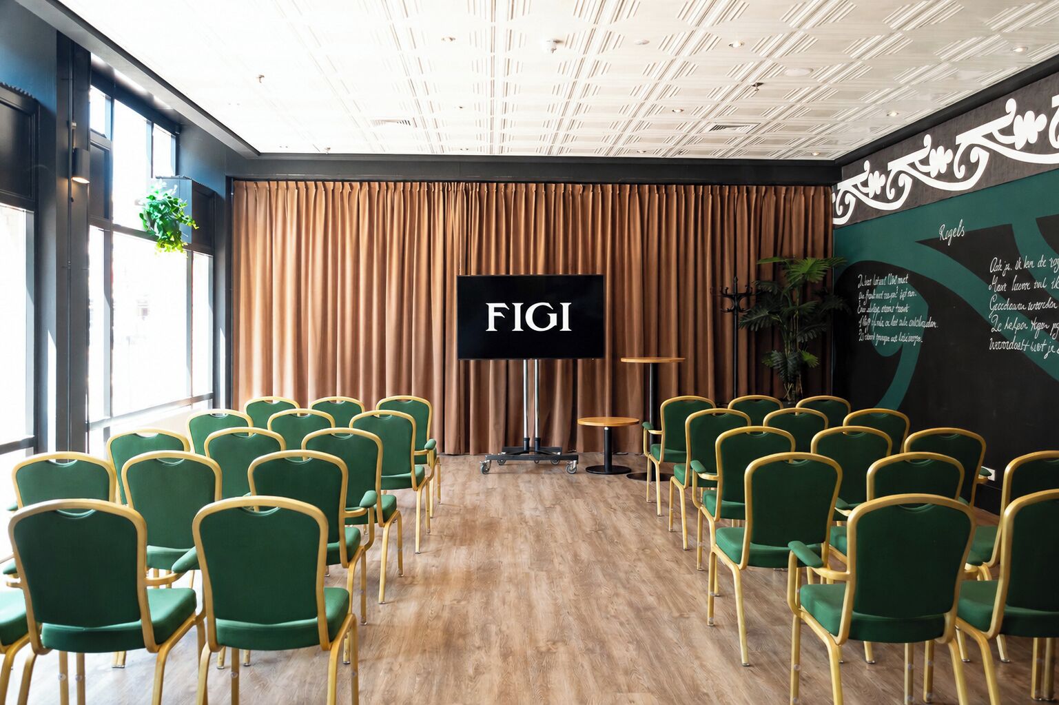Un salón de conferencias con filas de sillas verdes, una pantalla grande que muestra 'FIGI' y suelo de madera.
