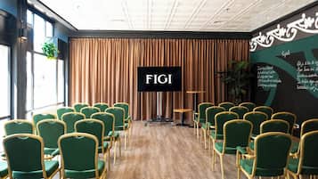 Un salón de conferencias con filas de sillas verdes, una pantalla grande que muestra 'FIGI' y suelo de madera.