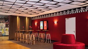 A modern interior with a red wall, wooden tables, and a red ottoman. - Hotel Theater Figi (Zeist)