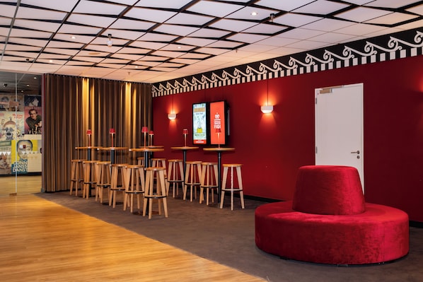 A modern interior with a red wall, wooden tables, and a red ottoman. - Hotel Theater Figi (Zeist)