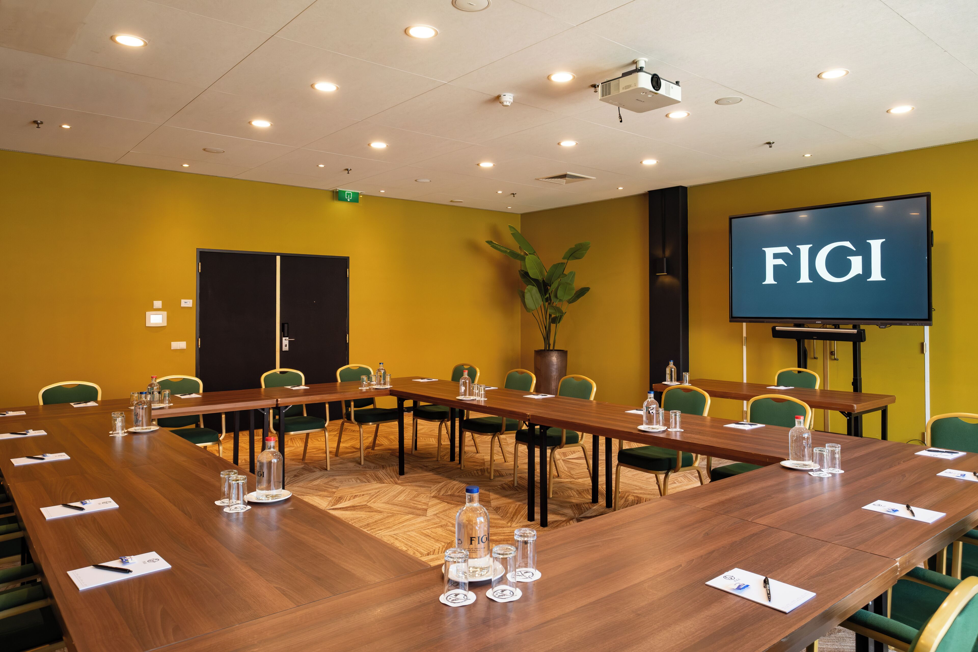 A conference room with a long table, chairs, a projector, and a screen displaying 'FIGI'.