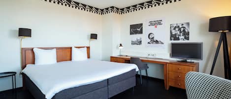 A hotel room with a bed, desk, chair, television, and wall decorations.