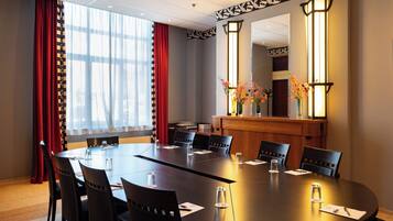 Een vergaderruimte met een lange tafel, stoelen en een receptiebalie met een bloevas.