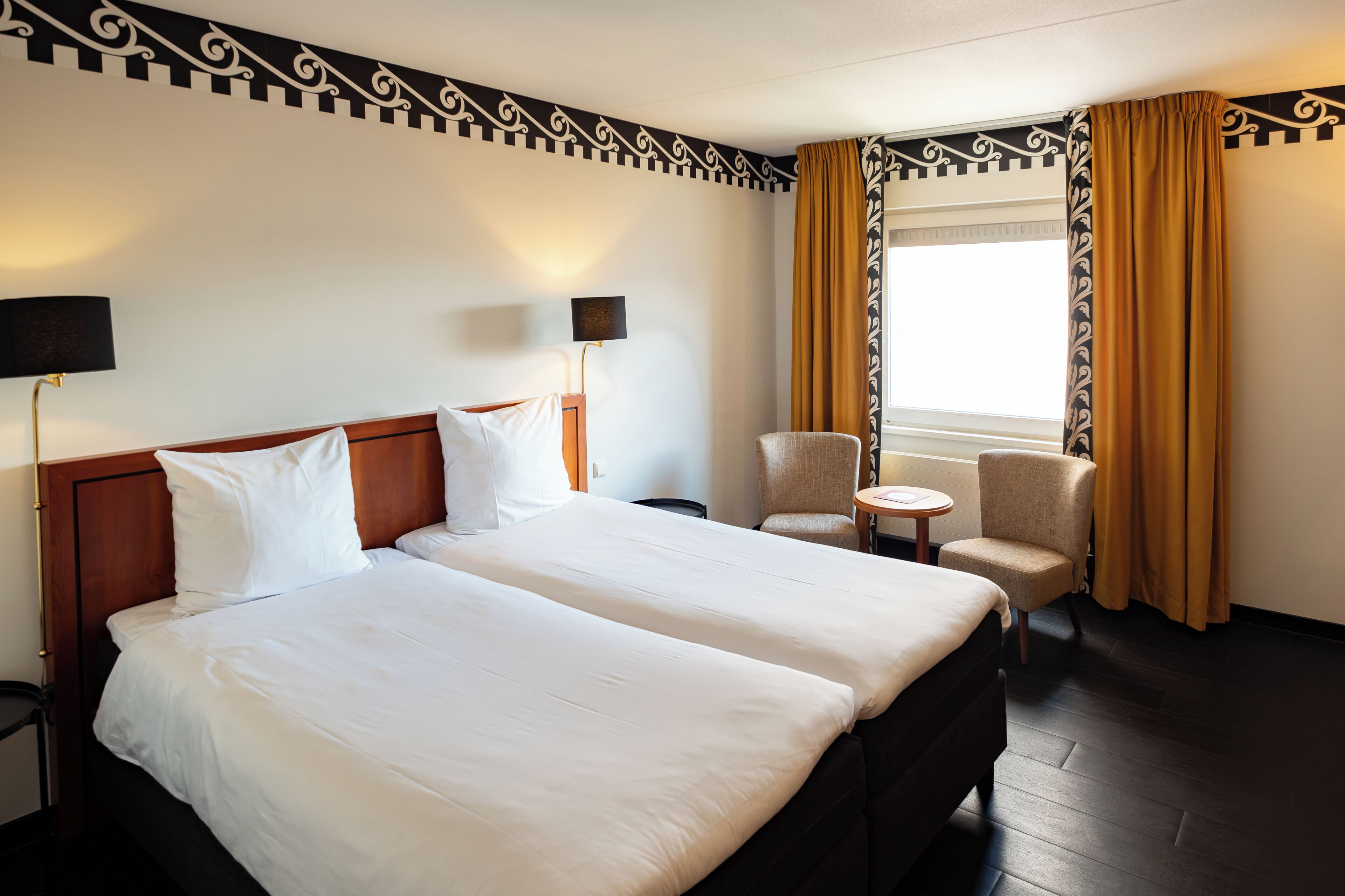 Habitación de hotel con dos camas, una mesita redonda pequeña, una silla y una ventana con cortinas.
