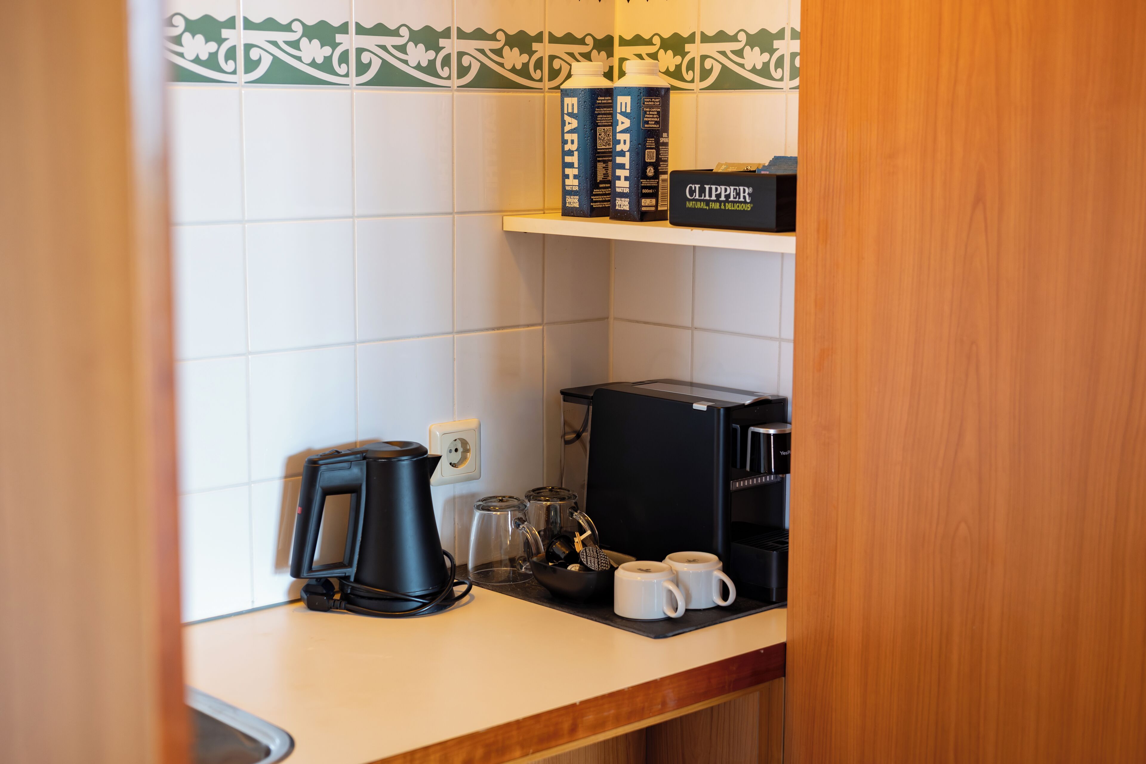 Een kitchenette met een koffiezetapparaat, een waterkoker en een koffiemachine. Op het aanrecht staan ook twee mokken.