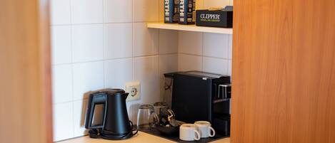 Una kitchenette equipada con cafetera, hervidor y máquina de café. También hay dos tazas sobre la encimera.