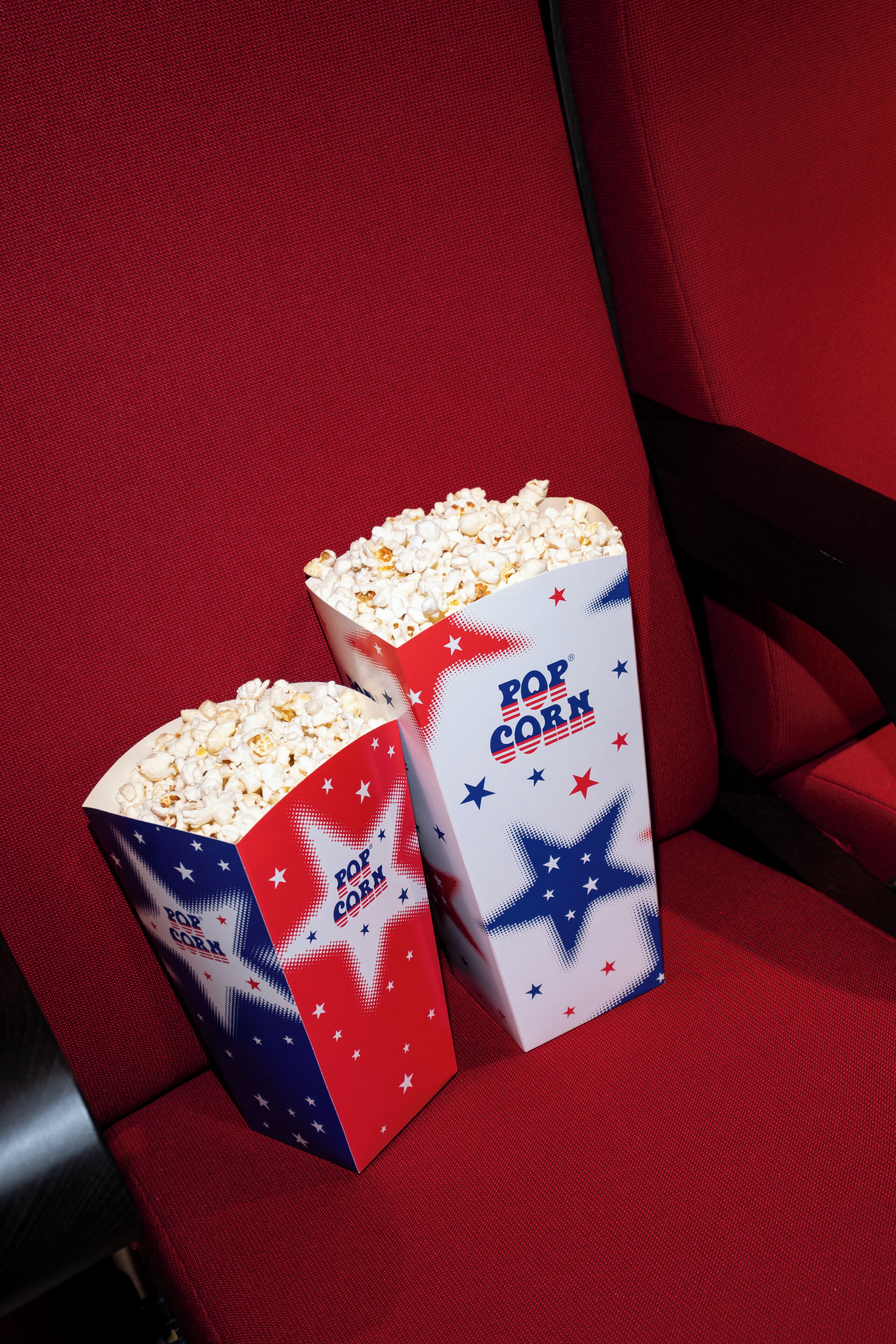Deux boîtes de pop-corn sur un siège rouge recouvert de tissu.