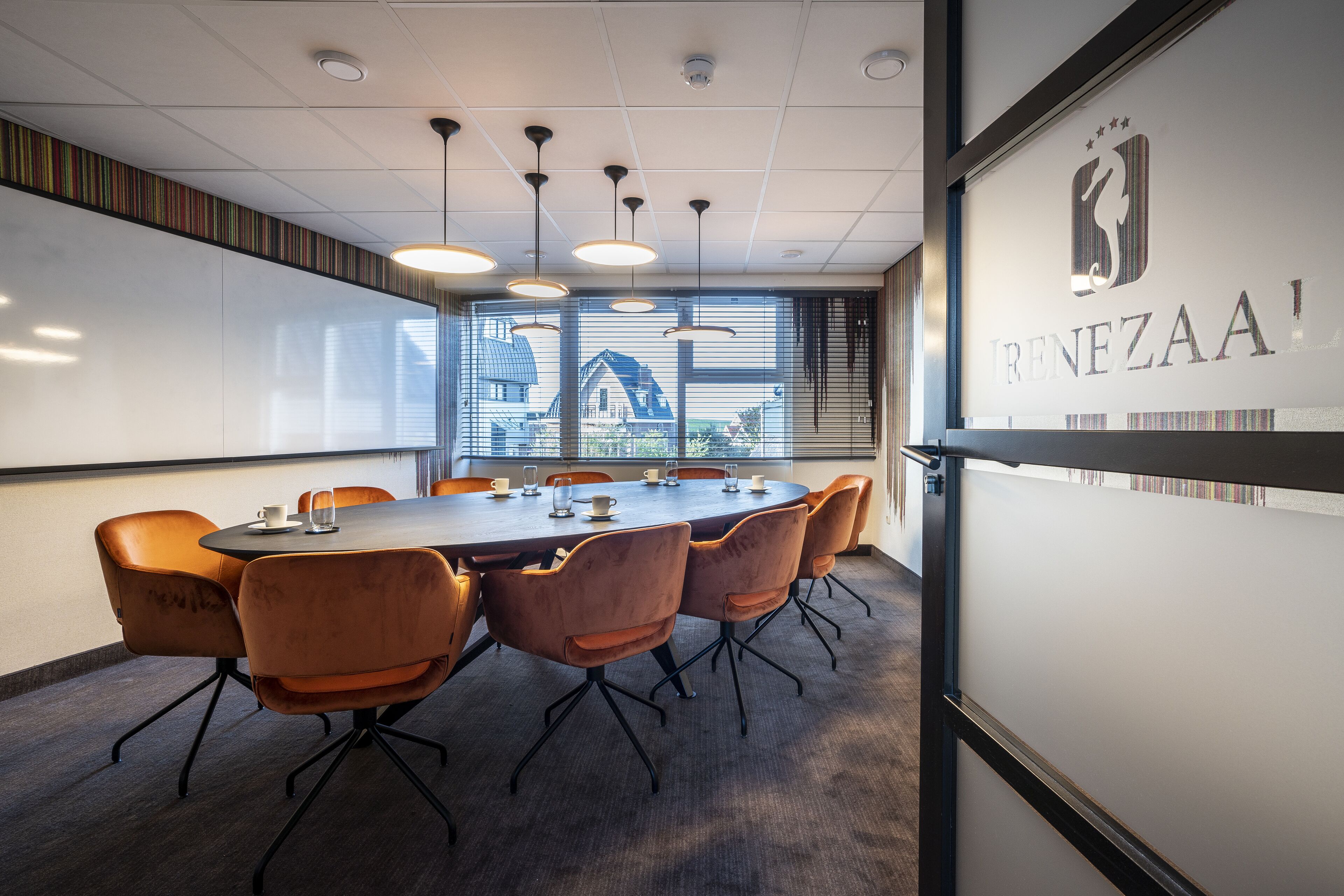 A conference room with a round table, six chairs, and a large window with blinds.