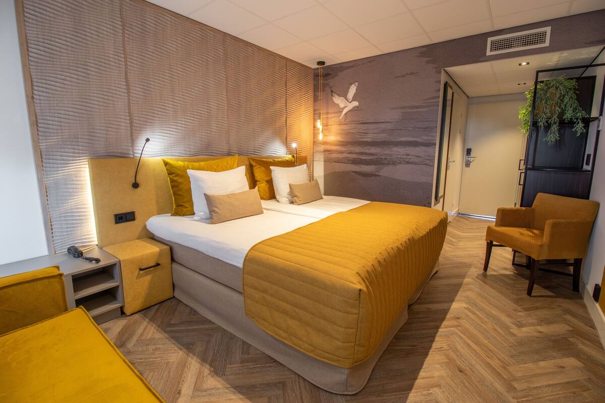 A modern hotel room with a large bed, bedside tables, a chair, and a plant.