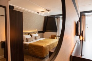 A modern hotel room with a large bed, a desk with a lamp, and a view of the outdoors through the window. - Grand Hotel Beatrix (Huisduinen)