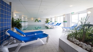 A pool area with blue and white lounge chairs, a tiled floor, and a glass wall. - Grand Hotel Beatrix (Huisduinen)