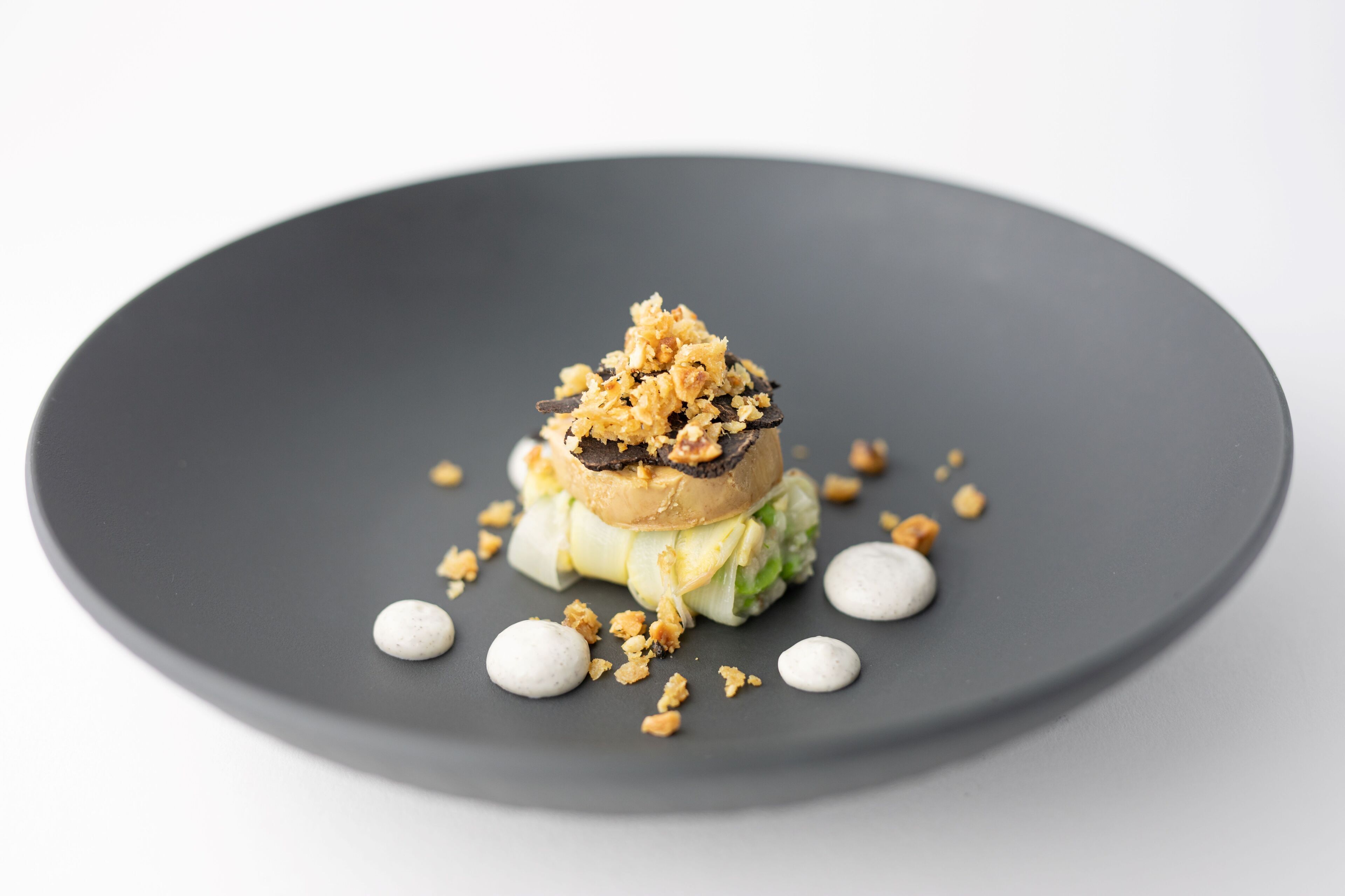 Een dessert op een donker bord, met een kruimelige topping en kleine witte bolletjes.