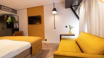 A hotel room with two beds, a sofa, a flat-screen TV, a small table with a plant, and a ceiling light.