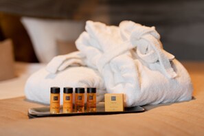 A bathroom with a white towel, a robe, and four bottles of body care products on a tray. - Grand Hotel Beatrix (Huisduinen)