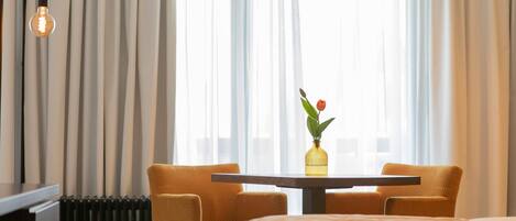 A hotel room with a bed, a table with two chairs, a vase with a flower, and a radiator.