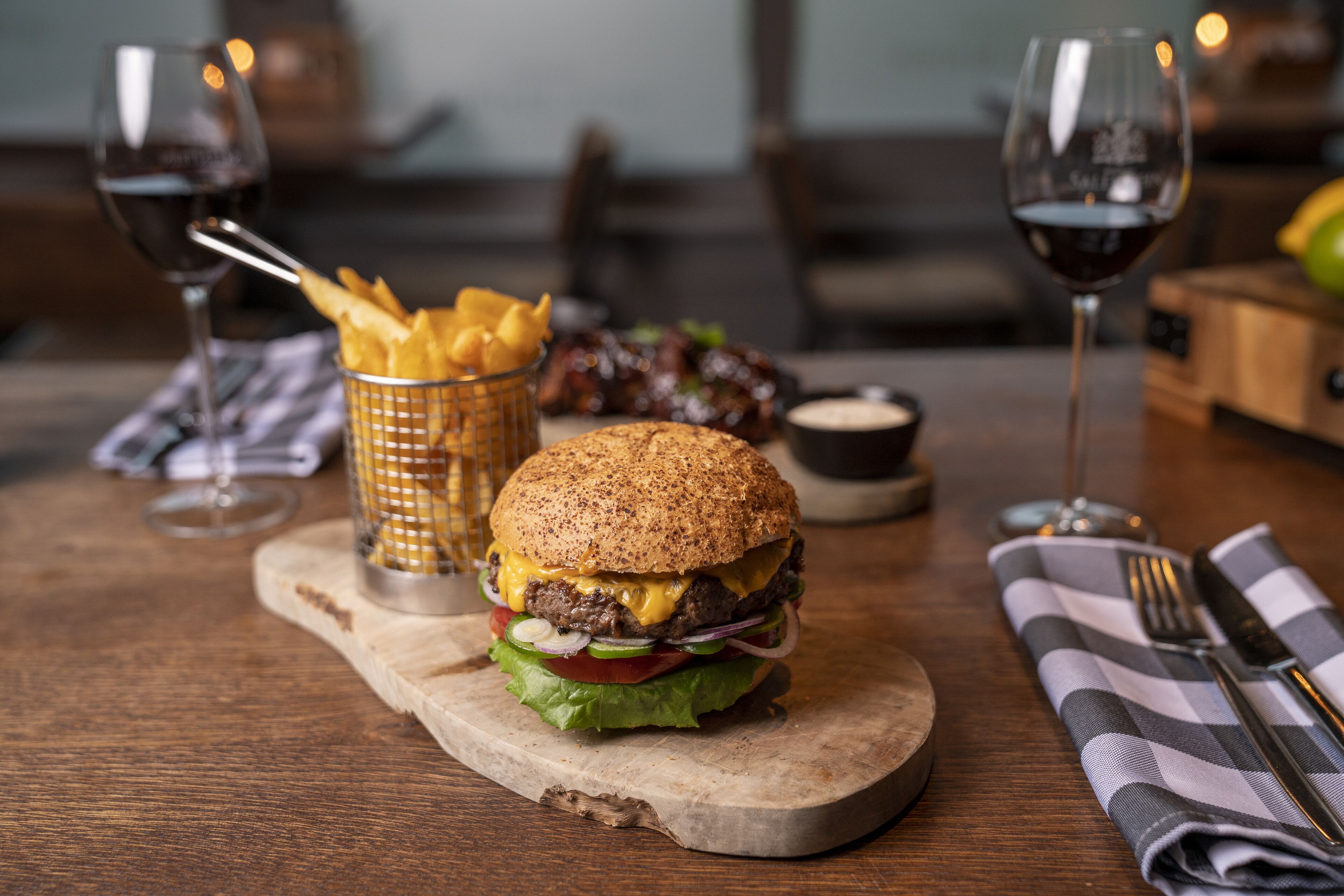 A burger with fries and a drink on a wooden board.