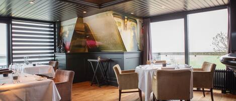 A restaurant with wooden floors, tables set for dining, and large windows offering a view.