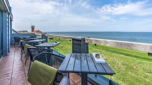 An outdoor patio with tables and chairs, overlooking a body of water and a distant tower. - Grand Hotel Beatrix (Huisduinen)