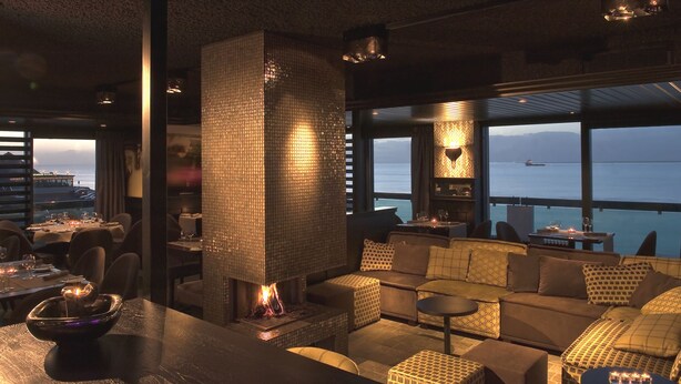 A cozy lounge area with a fireplace, comfortable seating, and a view of the ocean. - Grand Hotel Beatrix (Huisduinen)
