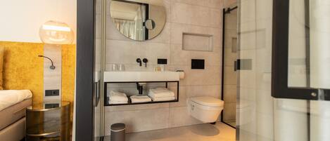 A modern bathroom with a glass shower enclosure, a round mirror, and a built-in sink with towel storage.