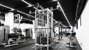A gym with various exercise machines, a mirrored wall, and a black and white color scheme. - Grand Hotel Beatrix (Huisduinen)