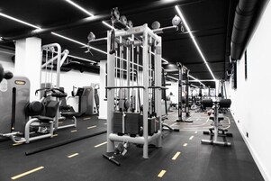 Un gimnasio con diversas máquinas de ejercicio, un espejo grande y una decoración en blanco y negro.