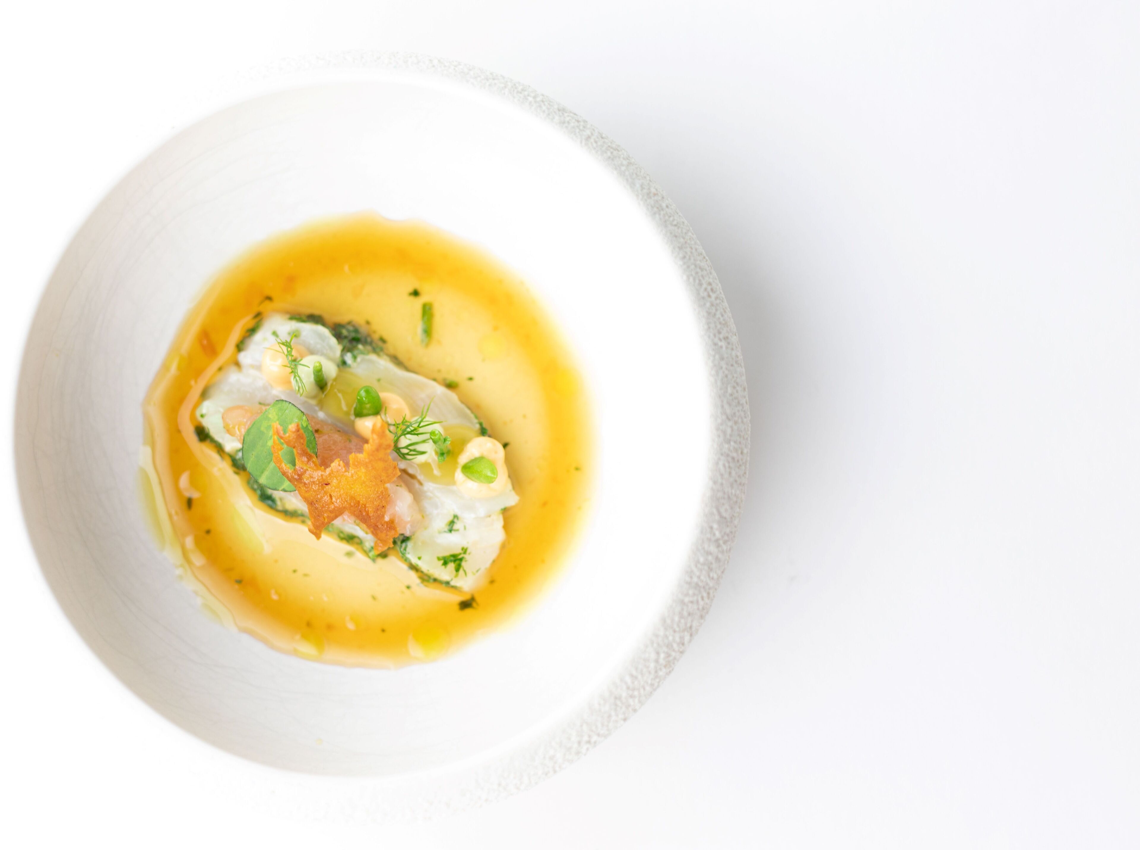 En hvid skål med en ret bestående af fisk, grøn pynt og en gylden sauce.