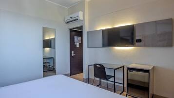Habitación de hotel con cama, escritorio, silla, televisor y aire acondicionado.