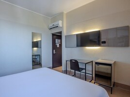 Habitación de hotel con cama, escritorio, silla, televisor y aire acondicionado.