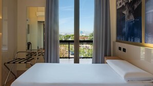 A hotel room with a bed, a view of the city through large windows, a balcony with a railing, and a wall-mounted air conditioning unit. - B&B Hotel Firenze Novoli (Florence)