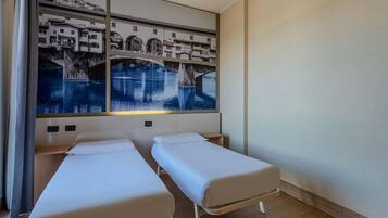 A hotel room with two single beds, a large wall-mounted artwork of a bridge over water, and a wooden floor.