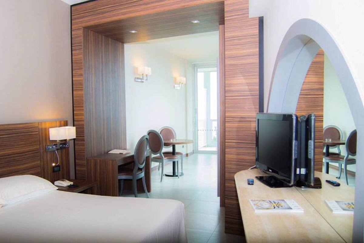 A hotel room with a bed, a desk with a TV, a chair, and a table.