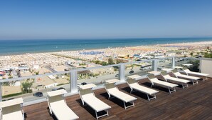 Terraço no telhado com espreguiçadeiras, vista para a praia e para a cidade.