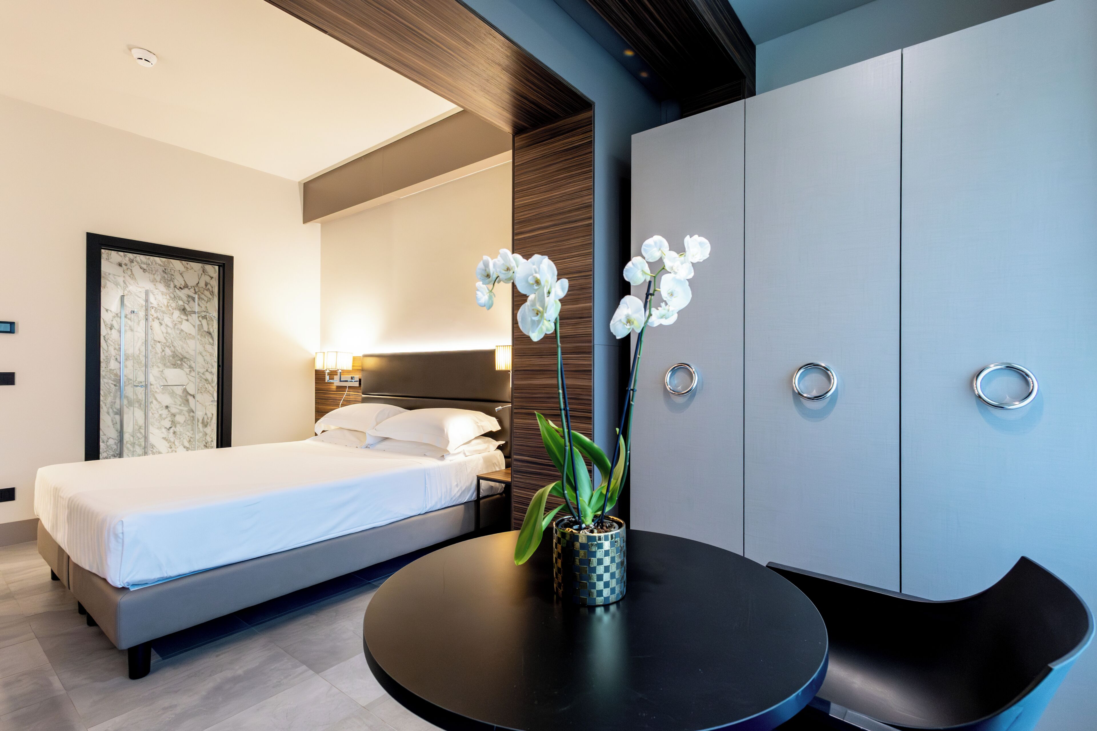 A modern bedroom with a bed, a round table with a vase of flowers, and a wardrobe.