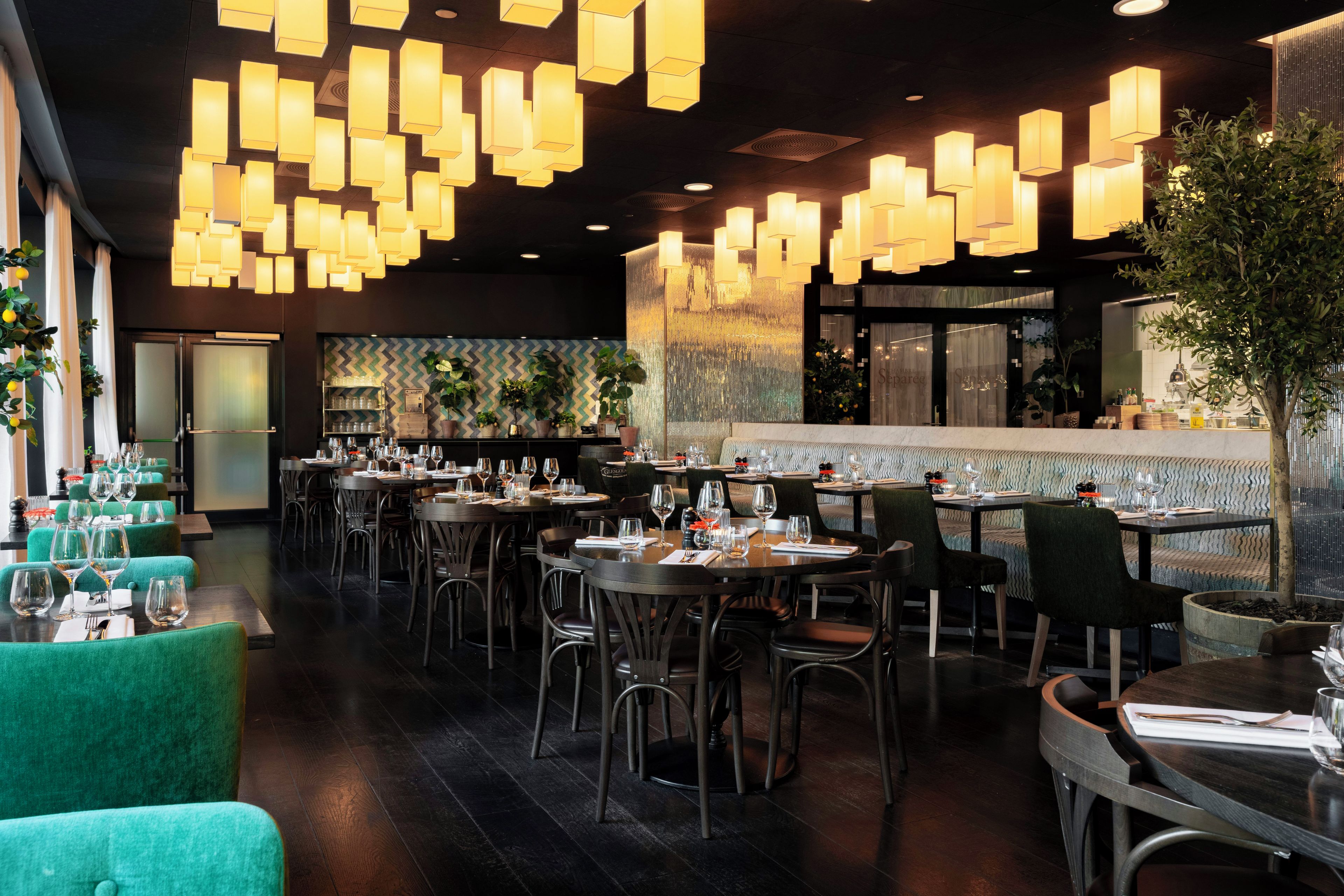 A restaurant interior with multiple dining tables, chairs, and hanging pendant lights.