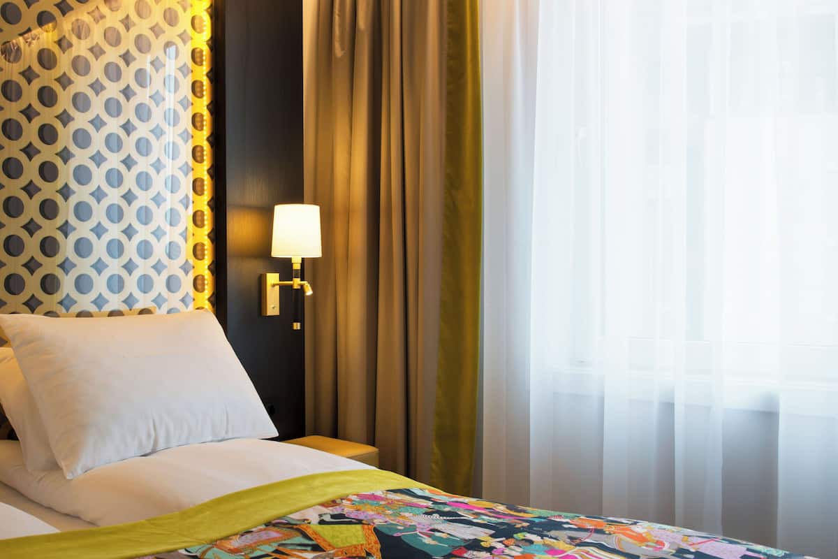 A hotel room with a bed, a nightstand, a lamp, and curtains.