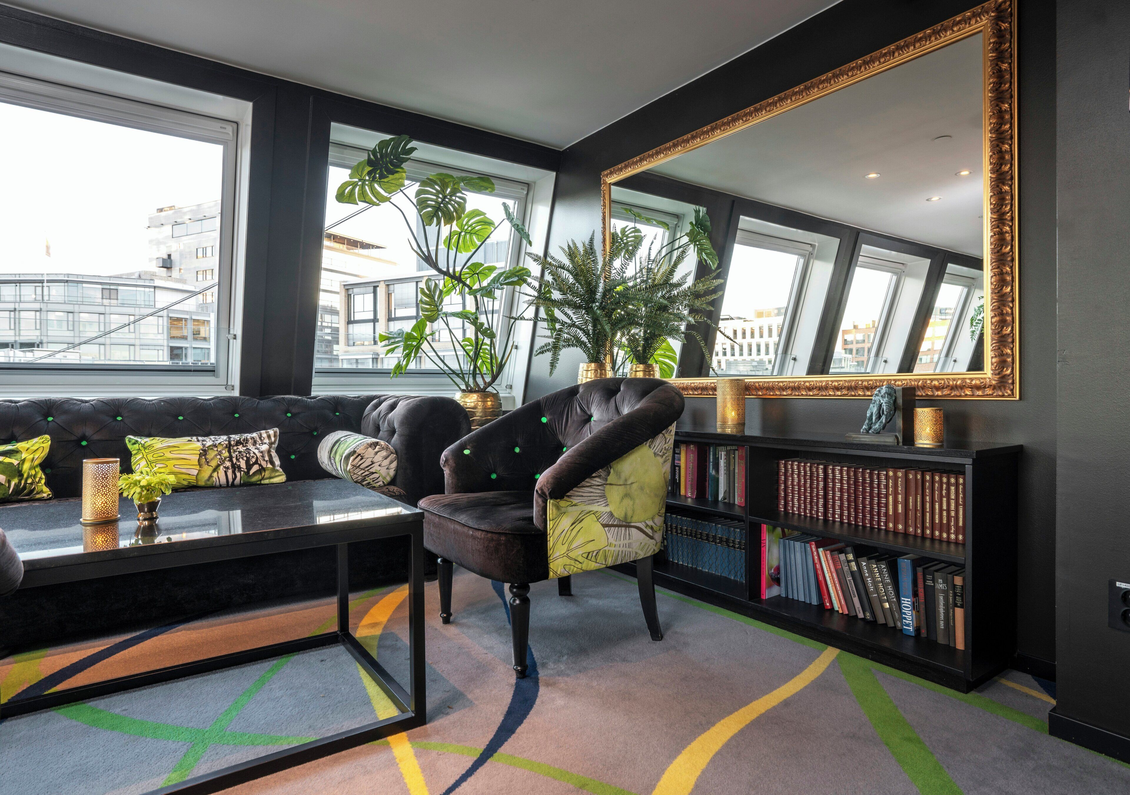 Una sala de estar moderna con un sillón de cuero, una estantería, un espejo grande y vistas de la ciudad a través de amplios ventanales.