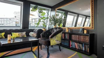 Una sala de estar moderna con un sillón de cuero, una estantería, un espejo grande y vistas de la ciudad a través de amplios ventanales.