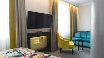 Habitación de hotel con cama, televisor montado en la pared, zona de estar con sofá y sillón, y mesa de vidrio con botellas.