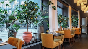 Ein Restaurantinneres mit Tischen, Stühlen, Blumentöpfen und Blick auf die Straße.