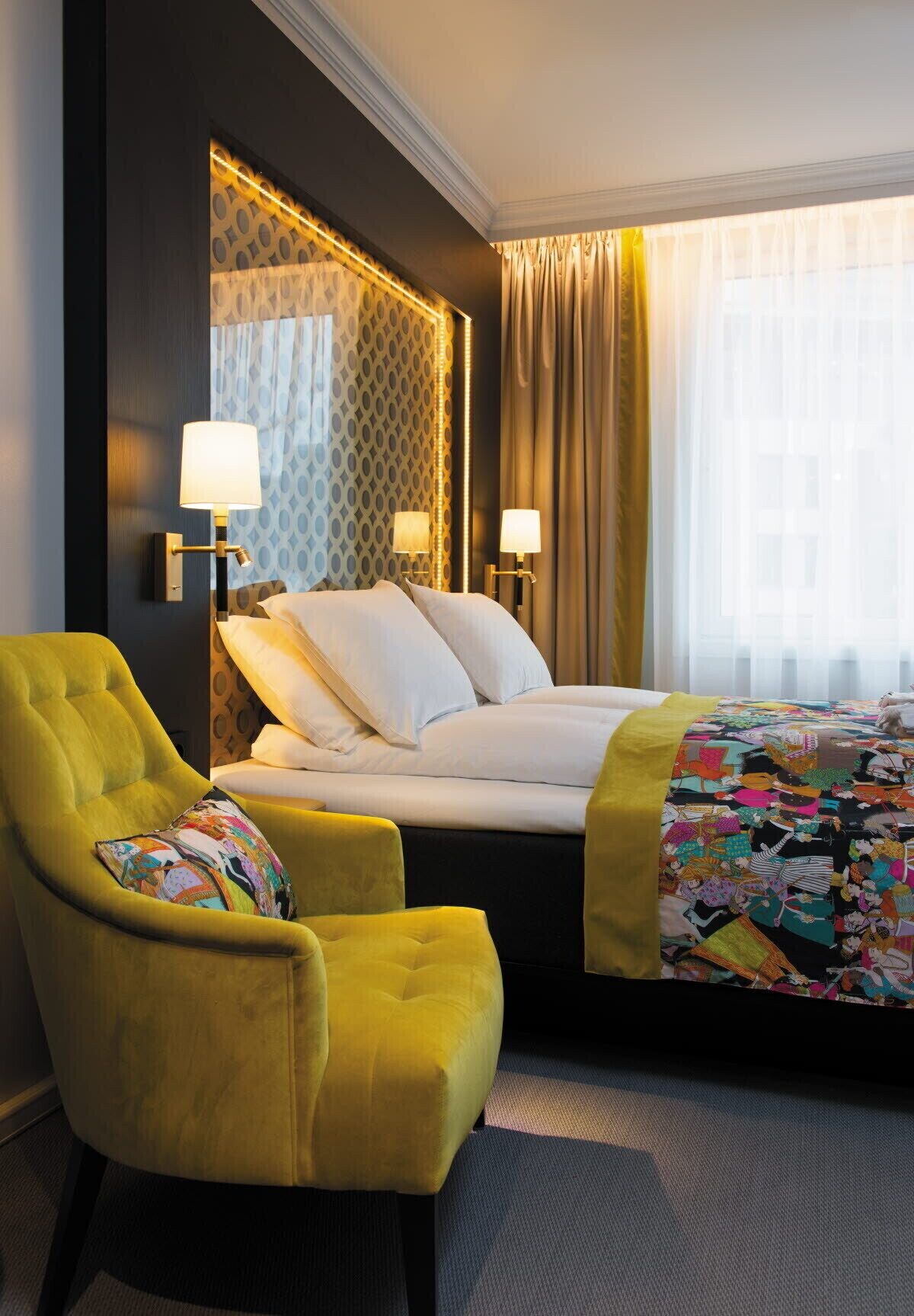 Green accent chair with multi colored pillow next to a bed with while linens and a colorful blanket