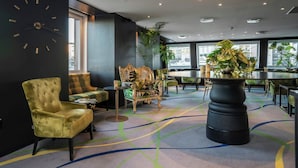Ein modernes Interieur mit einer großen Uhr, bequemen Sitzgelegenheiten, einem runden Tisch und bodentiefen Fenstern.