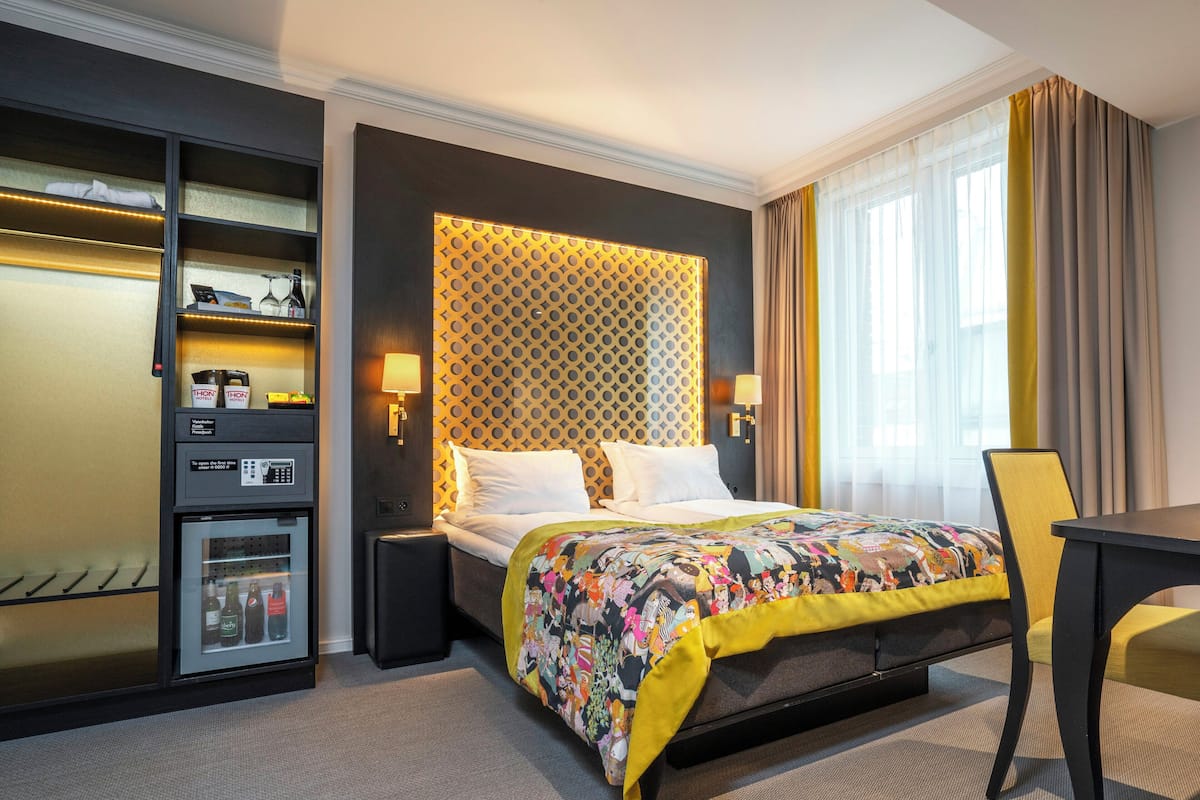 A hotel room with a bed, a desk, a wardrobe, and a minibar.