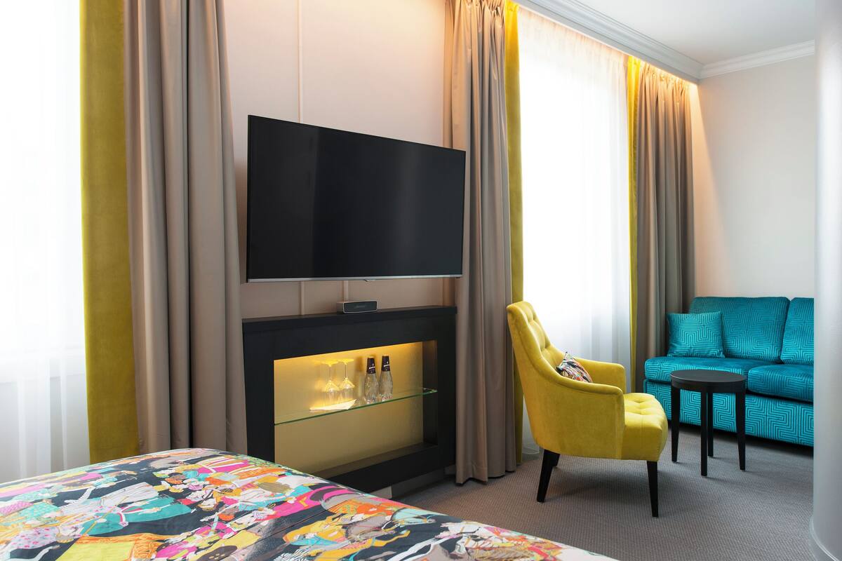 A hotel room with a bed, a TV mounted on a wall, a small table with a chair, and a sofa.
