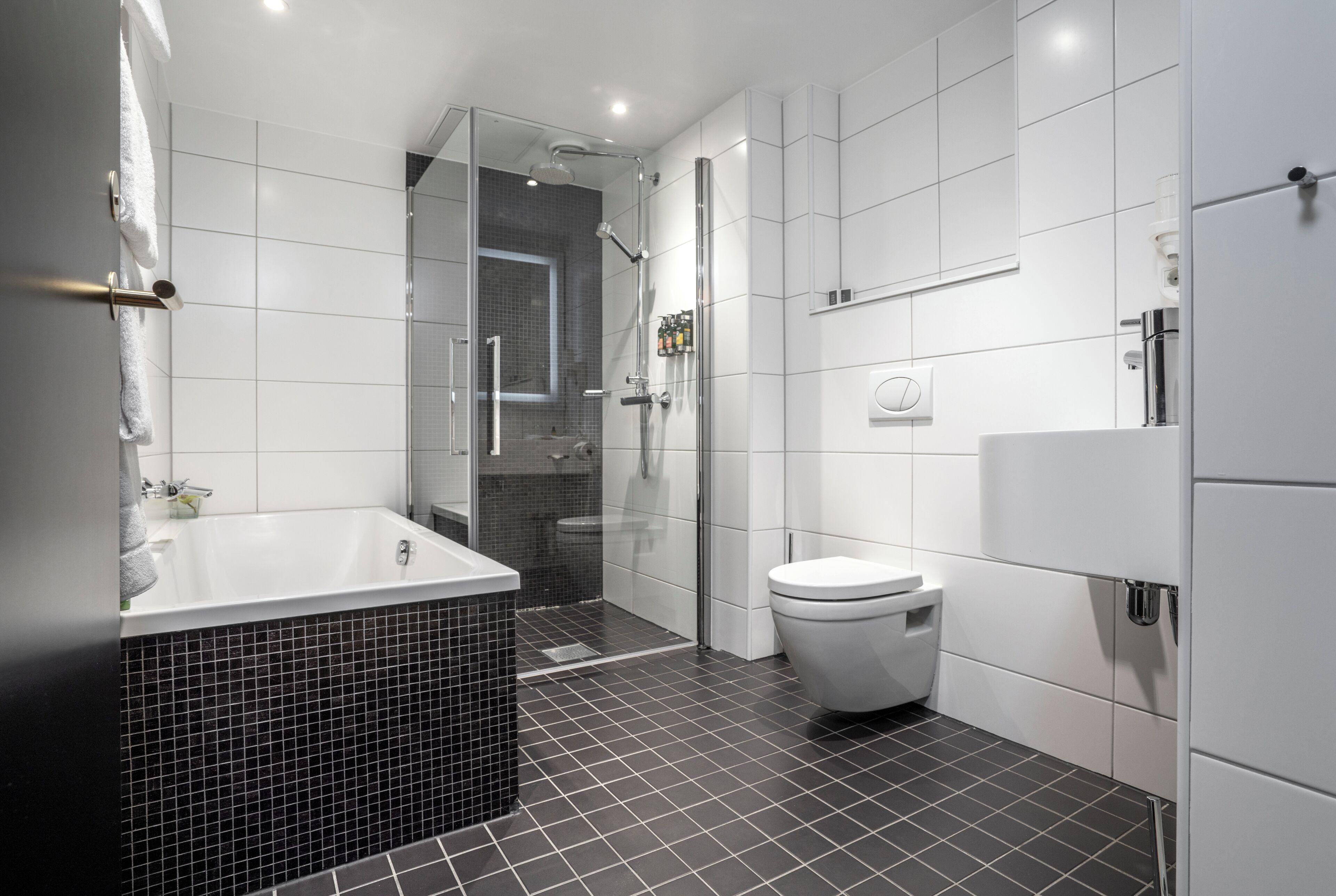 Een moderne badkamer met een douchecabine van glas, een wit toilet en een zwart betegeld bad.
